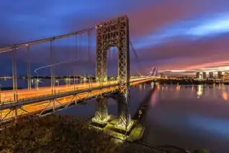 A stunning view of the San Francisco Bay Bridge at sunset, illuminated with city lights and a vibrant sky.