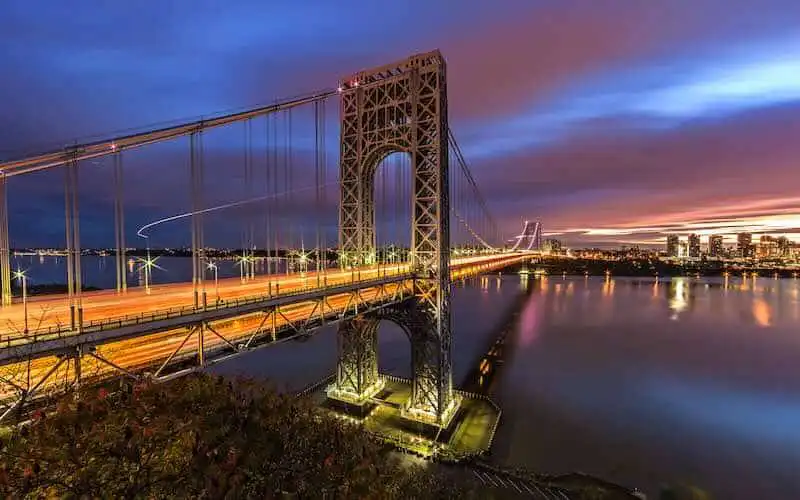 A stunning view of the San Francisco Bay Bridge at sunset, illuminated with city lights and a vibrant sky.