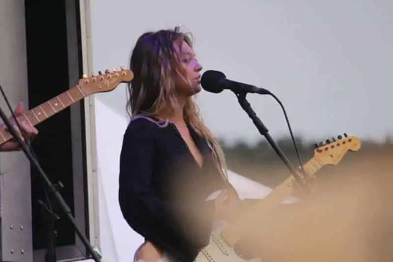 Close-up of a female musician singing and playing electric guitar at outdoor event.