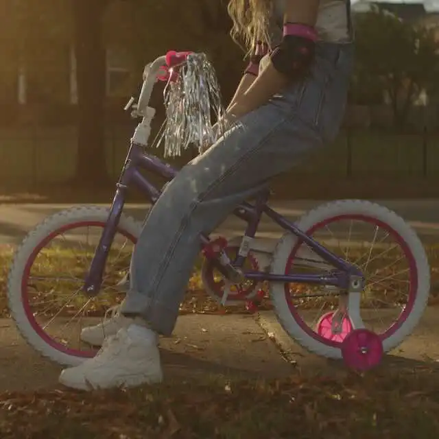 Young girl sitting on purple and pink bicycle with training wheels in park.