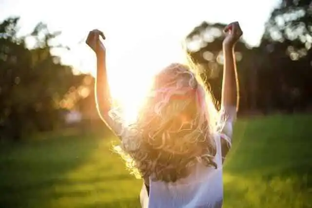 Happy woman raising arms in sunset field, celebrating freedom and positivity, natural outdoor scene.