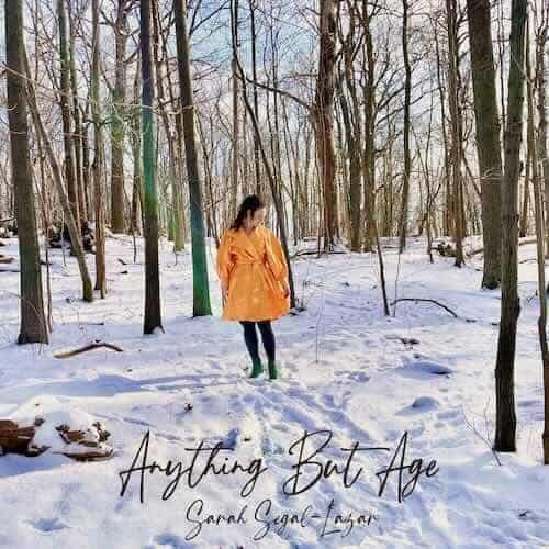 A person walking in a snowy forest wearing an orange coat.