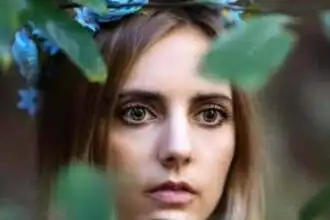 Close-up of a young woman with a floral headband, surrounded by greenery.