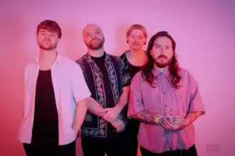 Diverse musical band group photo with vibrant pink background.