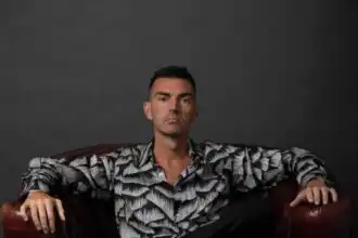 Male model with a serious expression, wearing a patterned shirt, against a gray background.