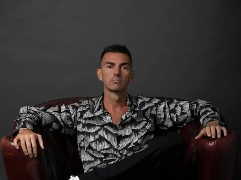Male model with a serious expression, wearing a patterned shirt, against a gray background.