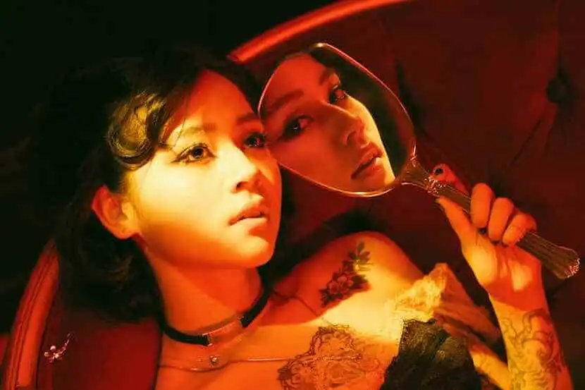 Close-up of two women lying on a bed, with one holding a hand mirror, emphasizing intimacy and allure.