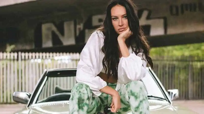 Portrait of a confident woman sitting on a car outdoors, casual fashion, natural setting.