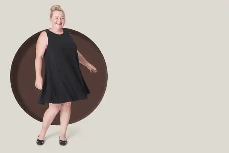 Happy woman in stylish black dress standing in front of a large chocolate circle background.