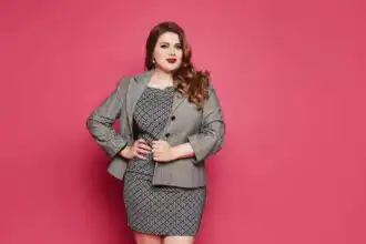 Empowered woman in business attire, standing confidently against a pink backdrop, representing professional success and confidence.