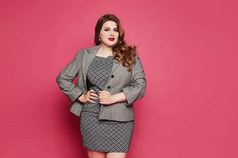 Empowered woman in business attire, standing confidently against a pink backdrop, representing professional success and confidence.
