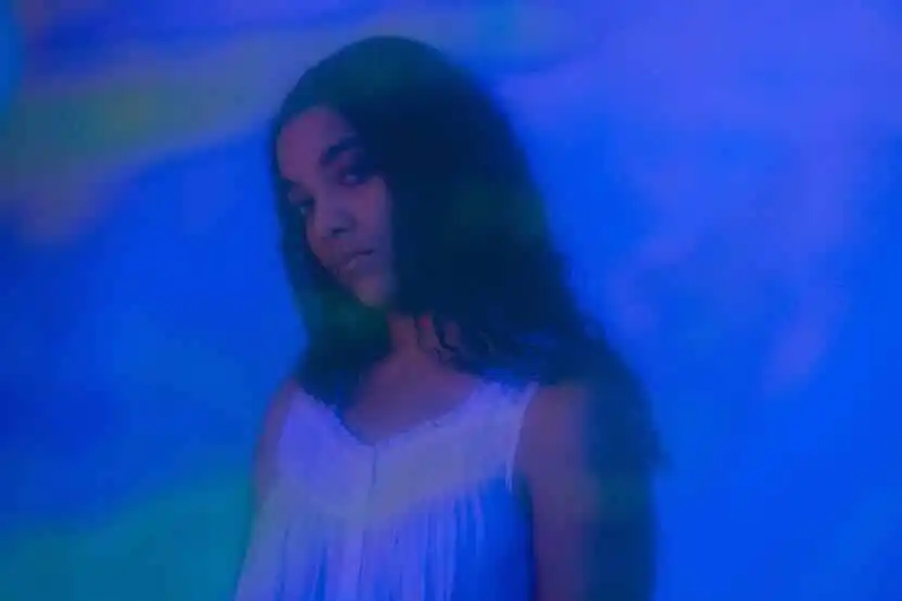 Portrait of a confident woman with dark hair under colorful lighting.