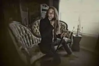 Intriguing person sitting on antique sofa, with finger to lips and holding cane, in a sophisticated vintage setting.