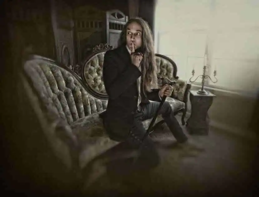 Intriguing person sitting on antique sofa, with finger to lips and holding cane, in a sophisticated vintage setting.