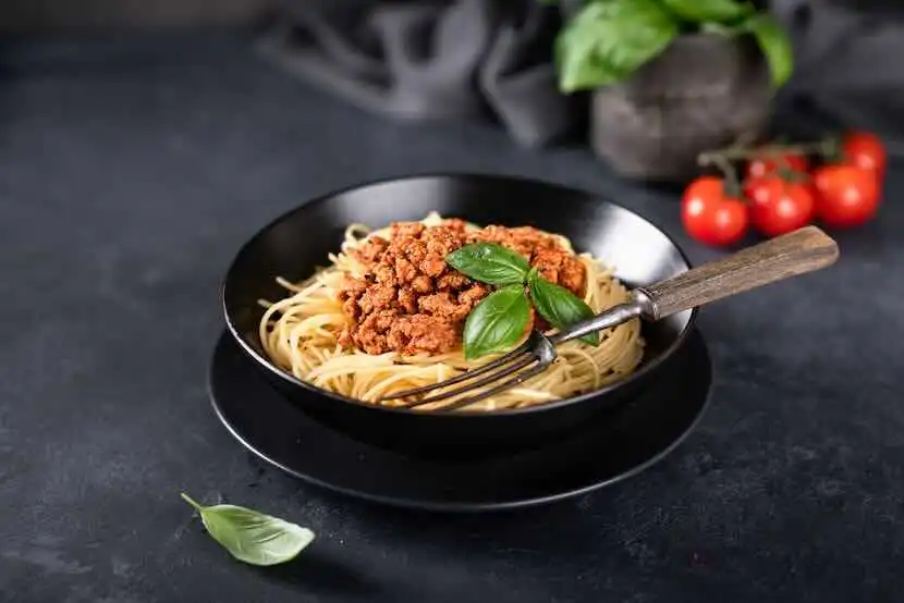 Delicious spaghetti topped with rich Bolognese sauce and fresh basil on a black ceramic plate.