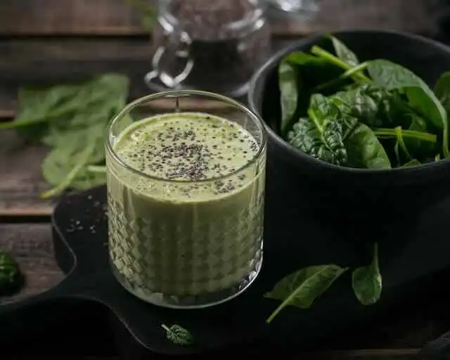 Bright green smoothie in a textured glass, fresh spinach leaves nearby, healthy detox drink.