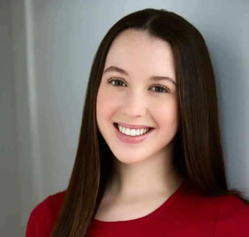 Young smiling woman with long brown hair in casual red top, showcasing confidence and beauty.