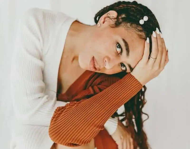 Close-up of a pensive woman resting her head on her hands, symbolizing mental health and emotional reflection.