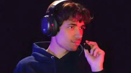 Young man wearing gaming headset, focused on gameplay, dark background.
