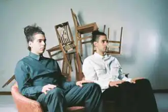 Men sitting on a pink velvet couch with stacked chairs in background.
