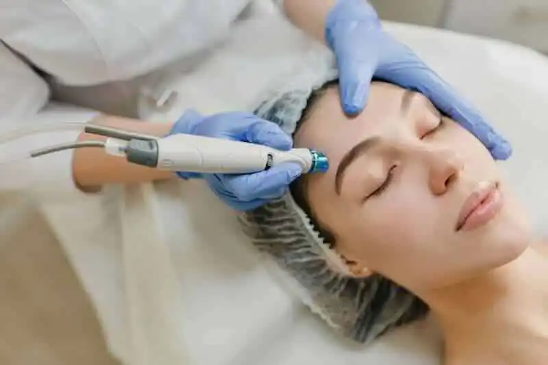 A woman receiving a professional facial treatment with a microdermabrasion device, emphasizing skincare and beauty services.