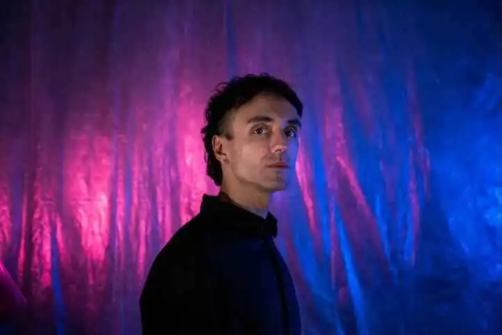 Elegant man with dark clothing against vibrant pink and blue background.