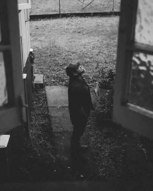 A person standing at night near a door in a dark outdoor setting, creating a peaceful and contemplative mood.