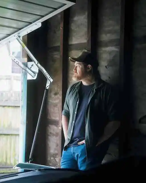 Man looking out of window in dimly lit room.