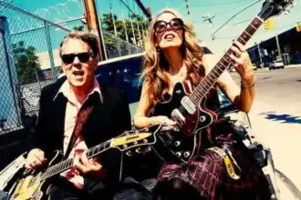 Vibrant image of a gay male and female musician playing guitars outdoors in an urban setting, showcasing LGBTQ+ pride and musical talent.