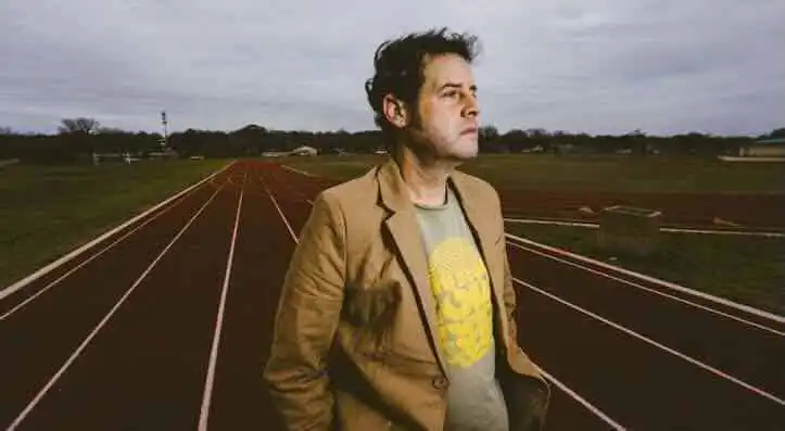 Reflective man on track at an outdoor stadium, contemplating life under cloudy skies.