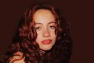 Stunning red-haired woman with voluminous curly hair and radiant makeup, showcasing confidence and elegance.