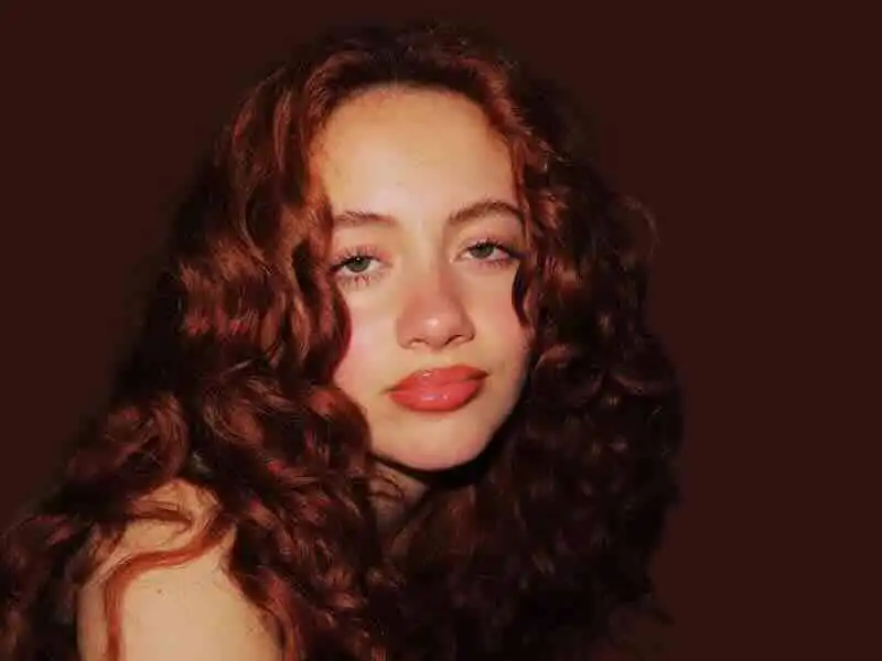 Stunning red-haired woman with voluminous curly hair and radiant makeup, showcasing confidence and elegance.