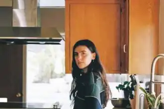 Young woman with dark hair at home kitchen counter, natural light, casual style, potted plants.