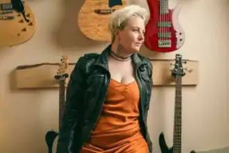 Young woman with short blonde hair and edgy style standing among guitars.