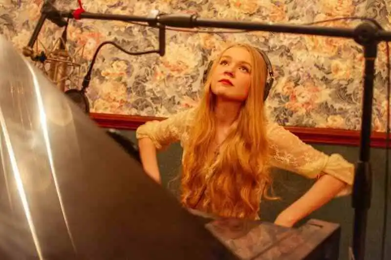 Alt text: Woman with long red hair wearing headphones in recording studio, focused on music.