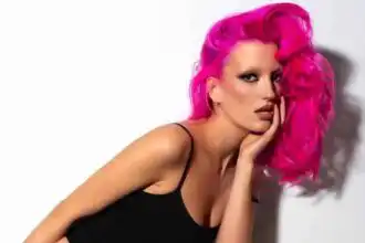 Bright pink hair styled in loose waves, bold makeup, and confident pose.