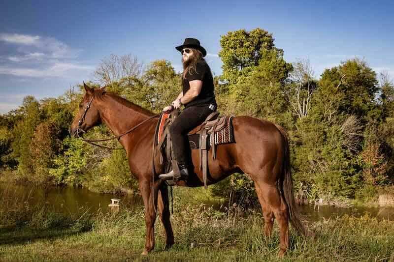 Outdoor horseback riding amid lush trees and blue sky.