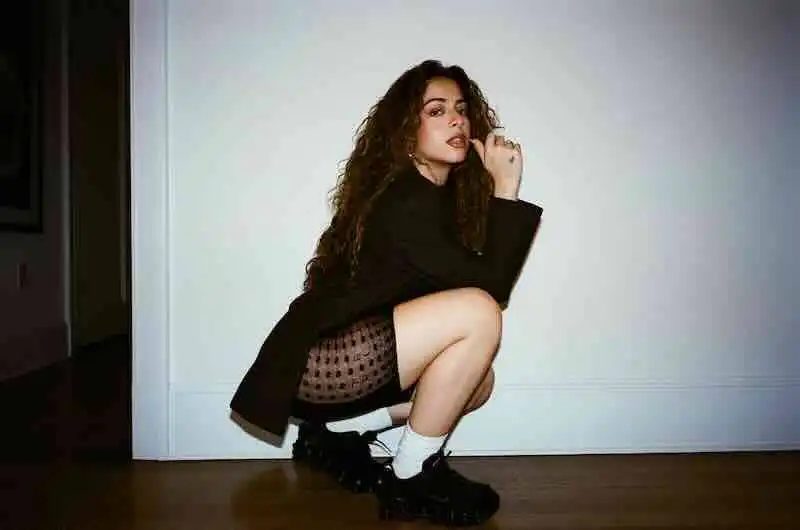 Fashion model crouching in stylish outfit, highlighting urban fashion trends and confident attitude.