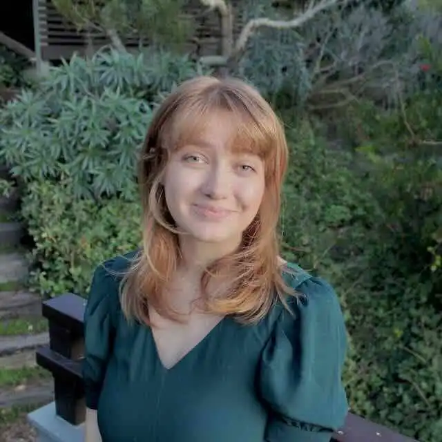 Young woman with red hair and a bright smile in a lush garden setting.