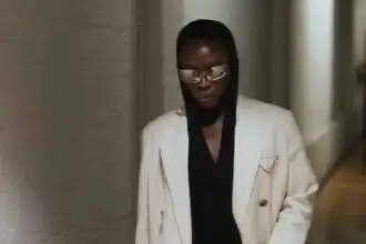 Stylish woman in white blazer and black hoodie, walking confidently in an urban setting.