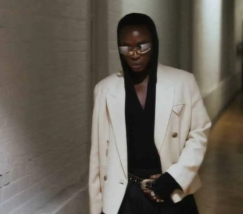 Stylish woman in white blazer and black hoodie, walking confidently in an urban setting.