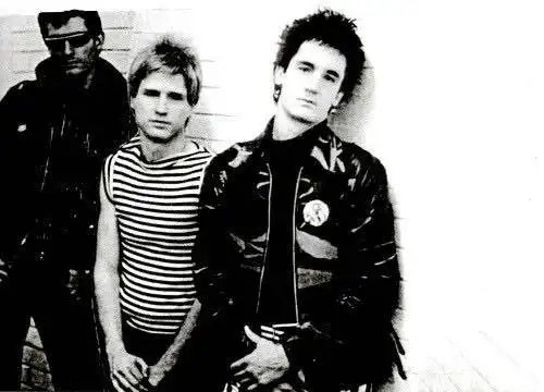 A black-and-white photo of three punk style musicians, with edgy fashion and confident expressions.