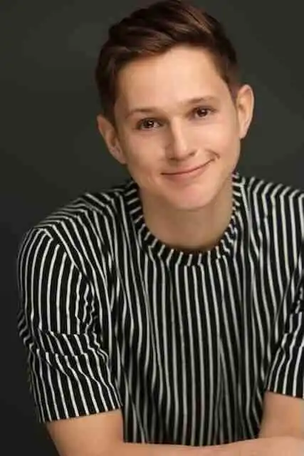 Young man with short brown hair and a striped black and white shirt smiling confidently.