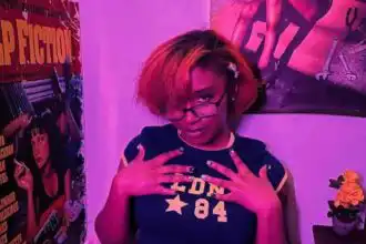 Portrait of confident woman with colorful hair and glasses in vibrant, artistic environment.