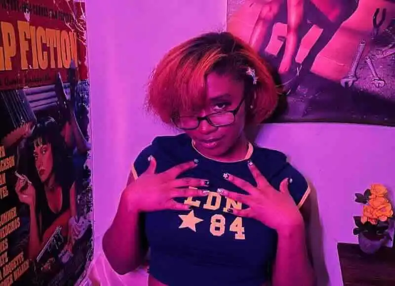 Portrait of confident woman with colorful hair and glasses in vibrant, artistic environment.