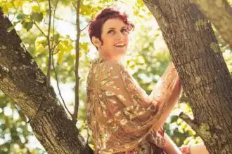 Happy woman outdoors hugging a tree in a sunny, leafy forest setting.