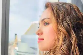 Close-up of a woman with wavy hair looking out a high-rise window, reflecting optimism and sophistication.