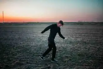 Young person dancing outdoors during sunset, embracing freedom and movement in a vast open landscape.