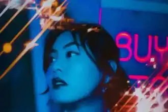A stylish woman with dark hair stands in a neon-lit city at night.