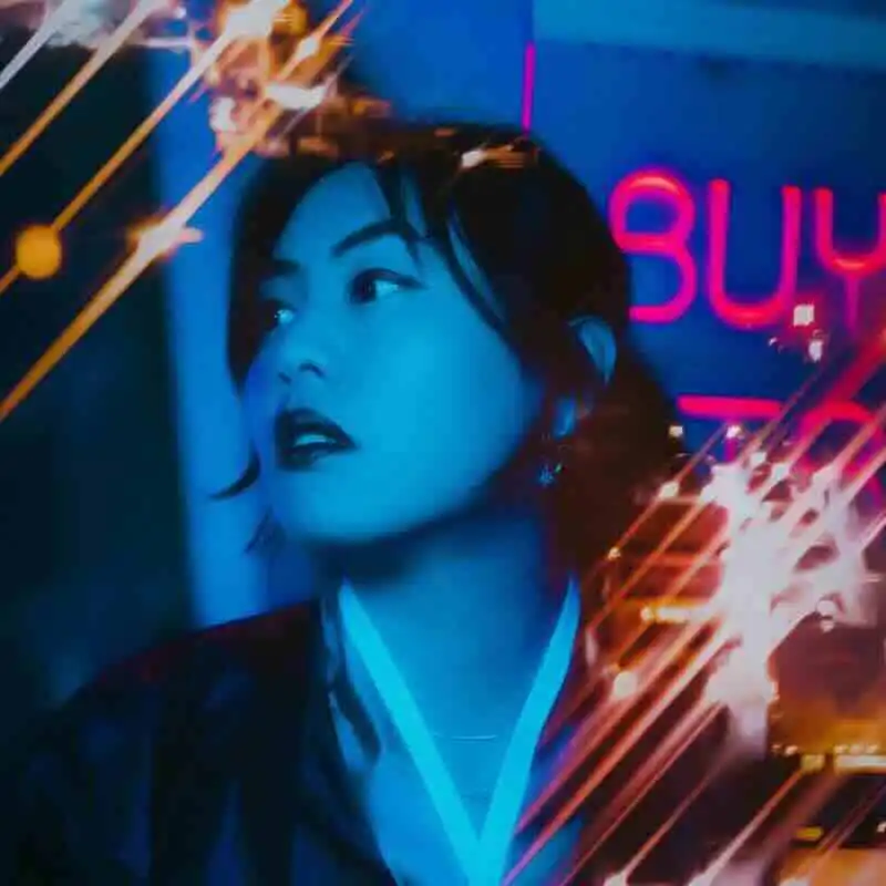 A stylish woman with dark hair stands in a neon-lit city at night.